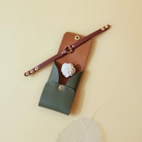 handmade green leather card holder with tan sheep leather lining and a maroon handmade leather wrist band on a pastel yellow background