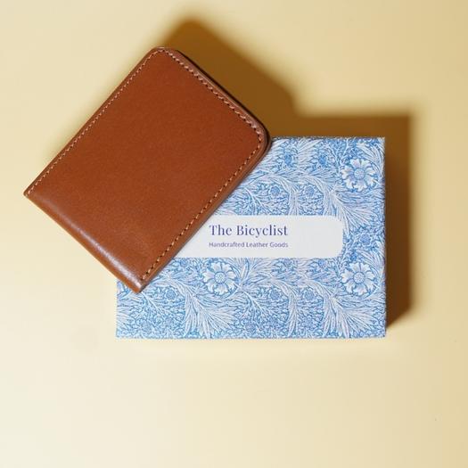Tan Brown leather wallet on a blue patterned box with 'The Bicyclist' label on a beige background