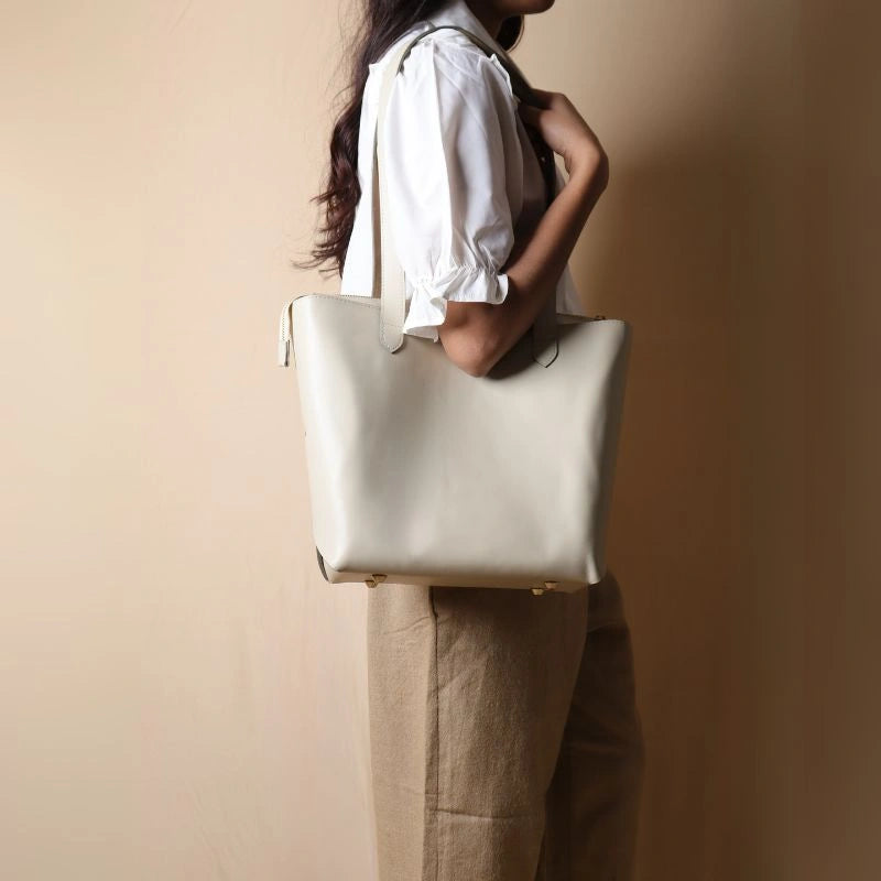 Woman in a white shirt carrying a white leather tote bag on her shoulder