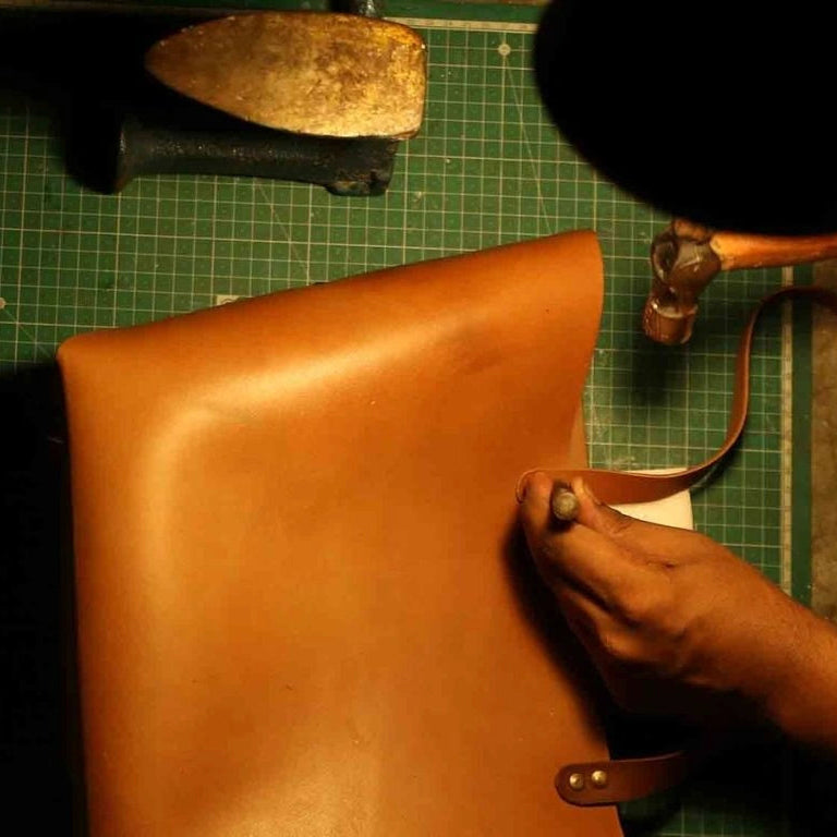 Craftsman making a leather tote bag with his tools around him
