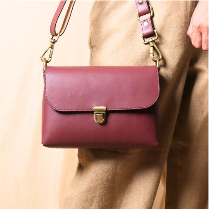 Woman in a beige trousers carrying a maroon leather crossbody shoulder sling bag with a flap in her hand