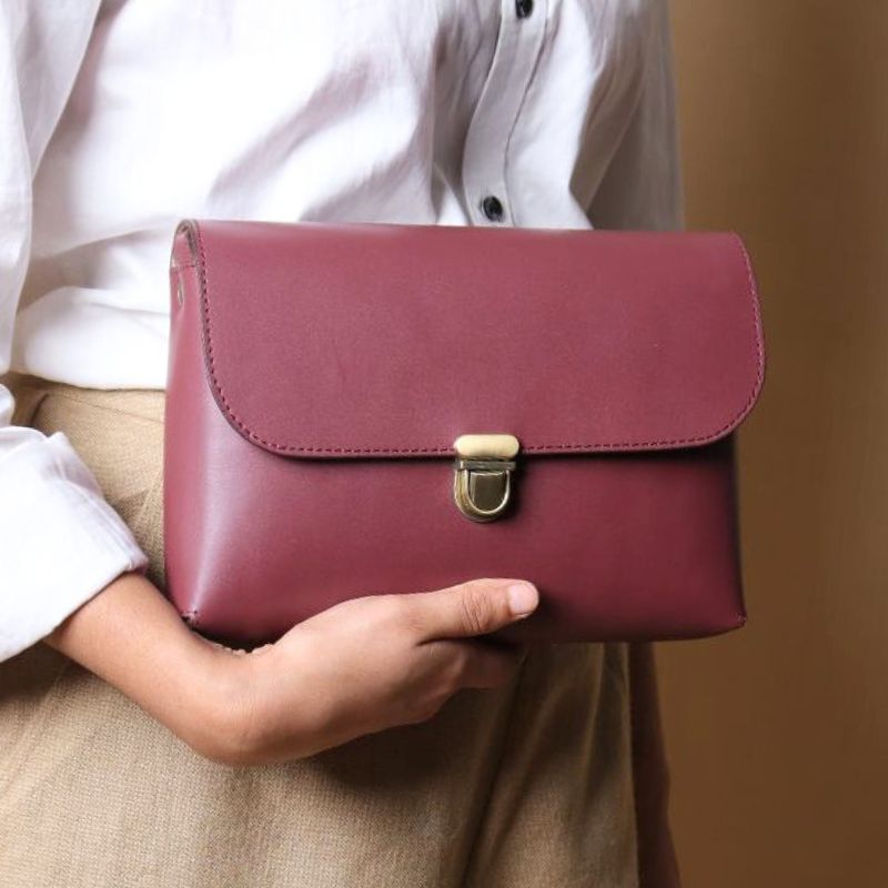 Woman in a white shirt carrying a maroon sling clutch bag in her hand with a flap and a light gold push lock