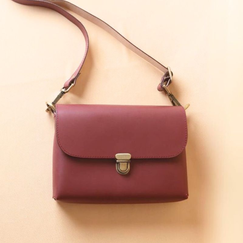 Top front view of a maroon leather crossbody sling bag with a flap and a light gold push lock
