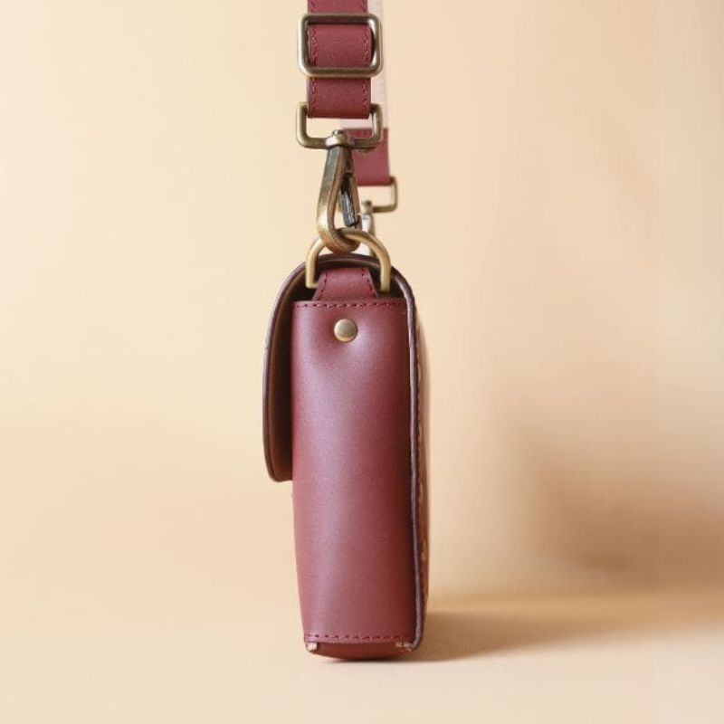 Side view of a maroon leather crossbody sling bag with a flap and soft gold fittings