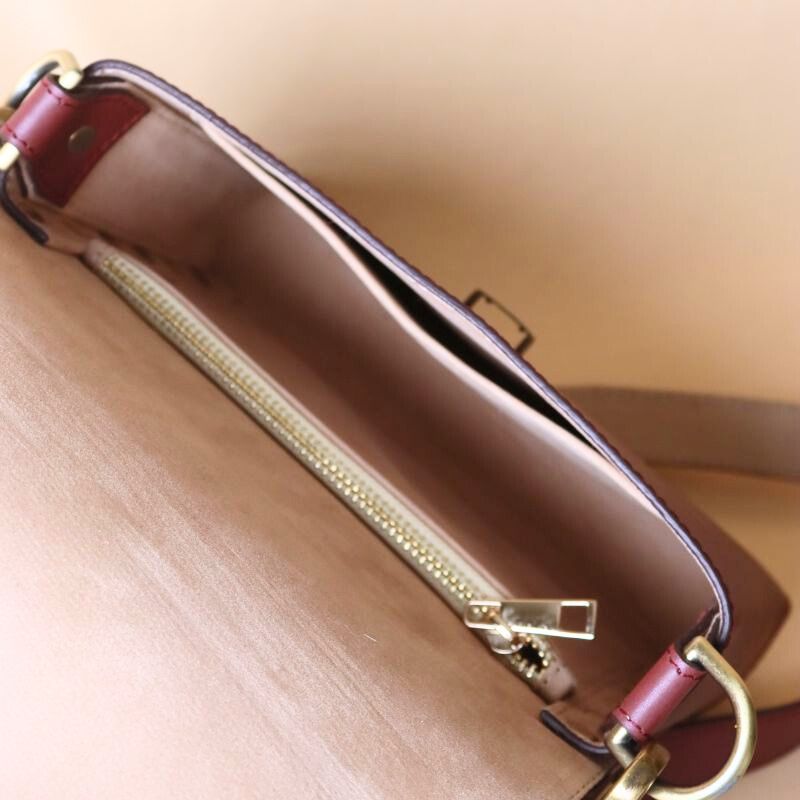 Top open and internal view of a maroon leather crossbody sling bag with a soft beige felt lining a zipped pocket and a open pocket