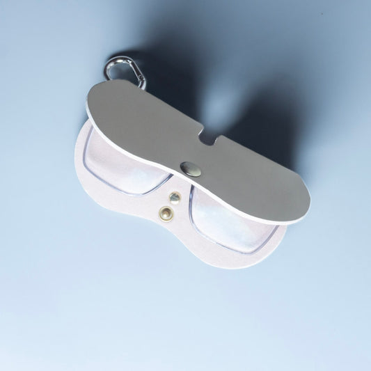 Half open view of a off white leather spectacle and eyeware protective sleeve with a pair of grey spectacles inside and a metal snap closure, made by 'The Bicyclist' featuring a chrome carabiner attached to the top right, set against a solid light blue background.