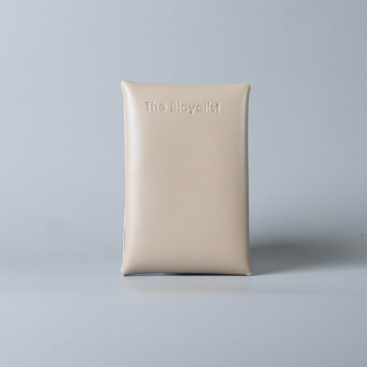Back side of a off white full grain leather card case with the brand name 'The Bicyclist' embossed at the top, set against a solid light gray background.