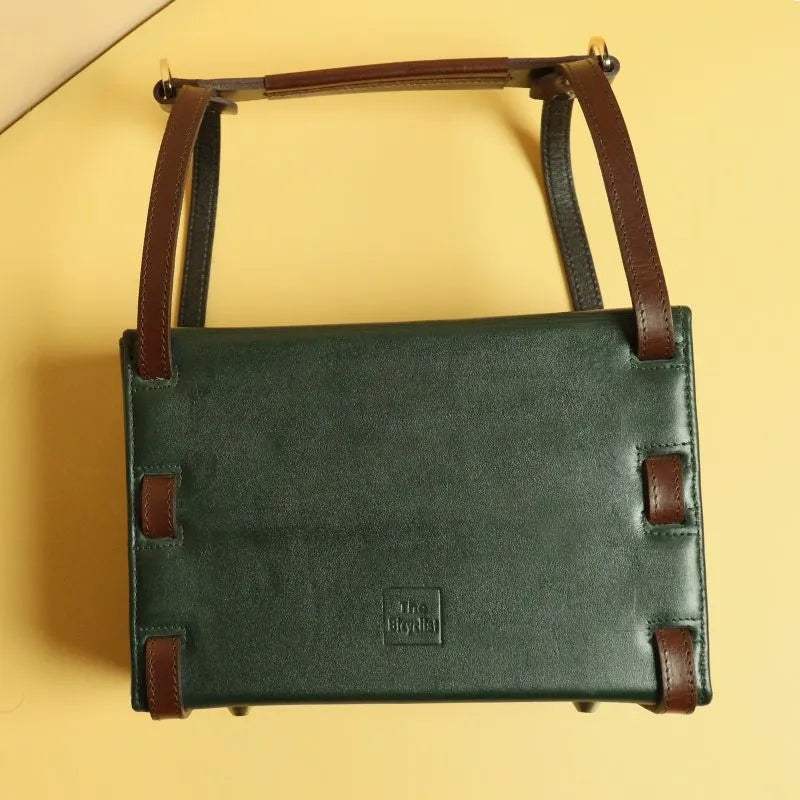 Rear view image of a dark green leather structured crossbody sling hand bag with removable dark brown leather straps, dark brown leather handle