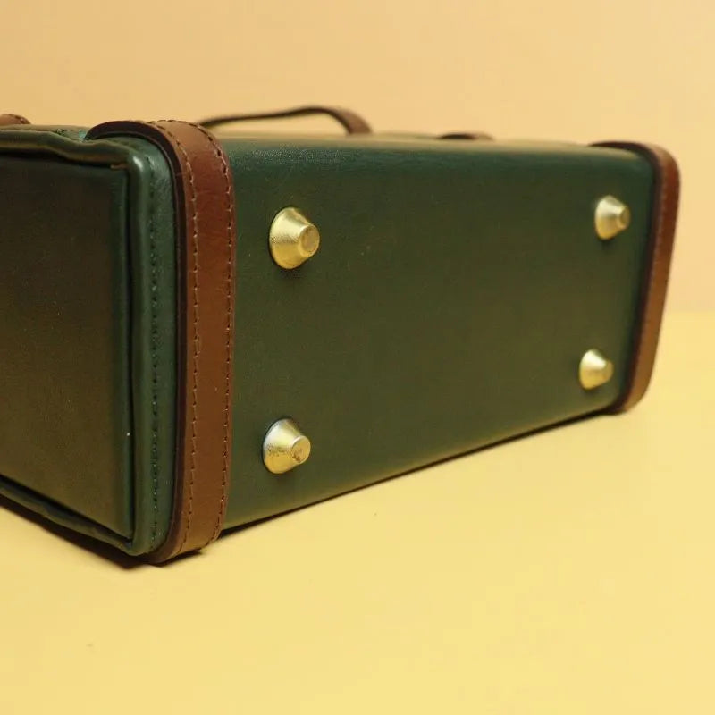 Bottom view image of a dark green leather structured crossbody sling handbag dark brown leather straps, and four light gold base studs