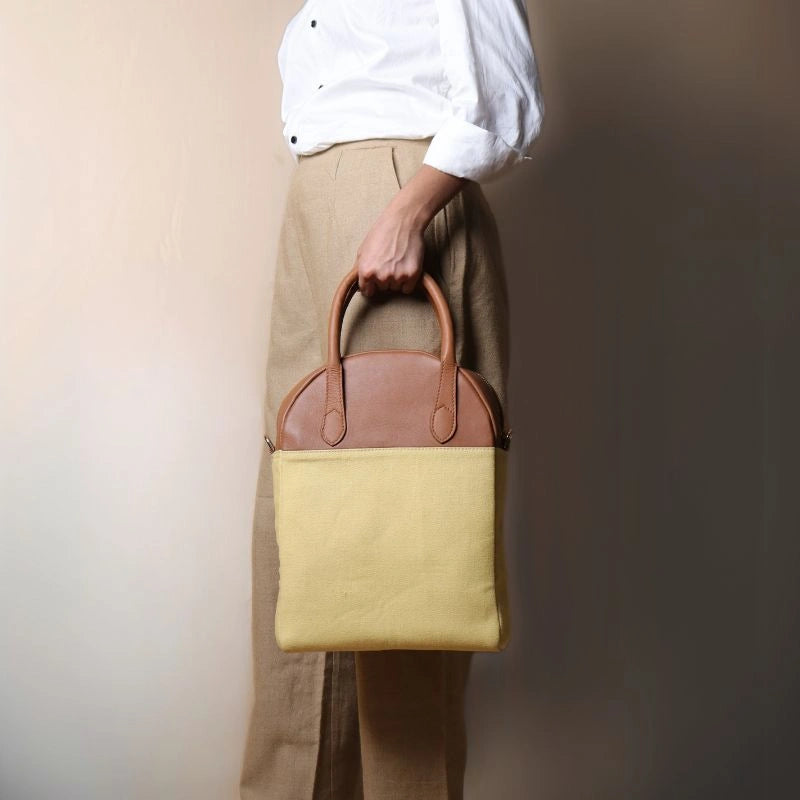 Woman in beige trousers holding a yellow canvas and tan handbag with handles in her hand
