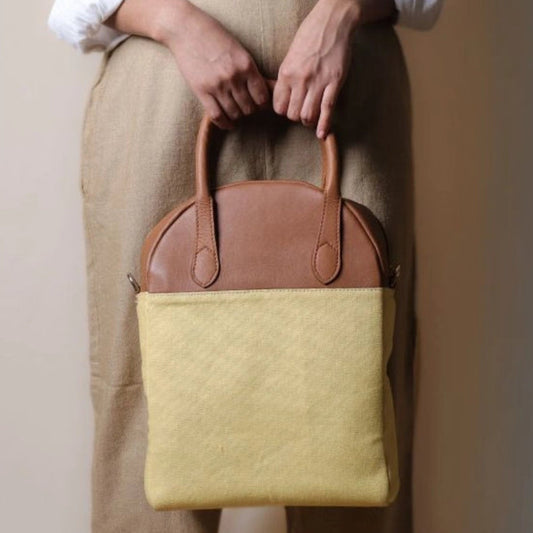 Woman in beige trousers holding a yellow canvas and tan handbag with handles in her hand