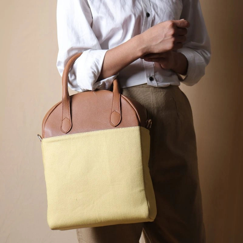 Woman in beige trousers holding a yellow canvas and tan handbag with handles in her hand