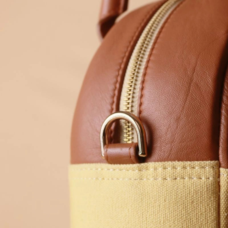 Detailed view of a golden fitting along with gold zip on a handbag with yellow canvas body and tan leather top