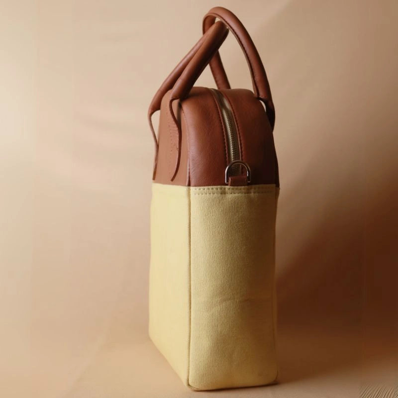 Side view of a unisex work handbag with yellow canvas body and tan leather top with gold fittings and a gold metal zip closure