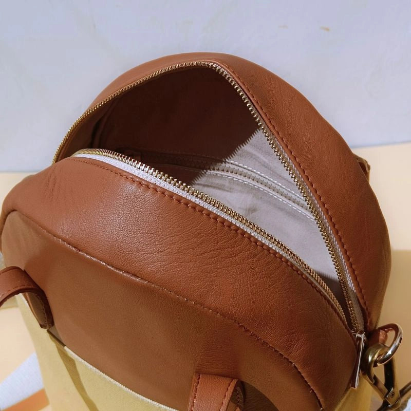 Top open internal view of a top handle yellow canvas and tan leather handbag with an internal zip pocket and a gold metal zip closure