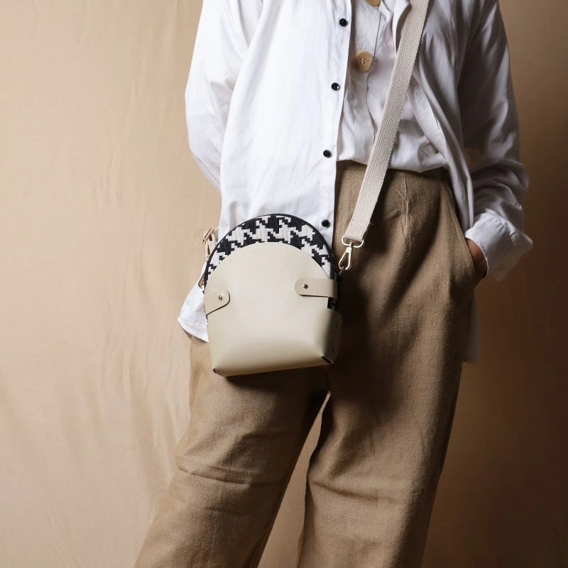 Woman in white shirt carrying over her shoulder a canvas bag with black and white houndstooth weave inside a off-white leather case