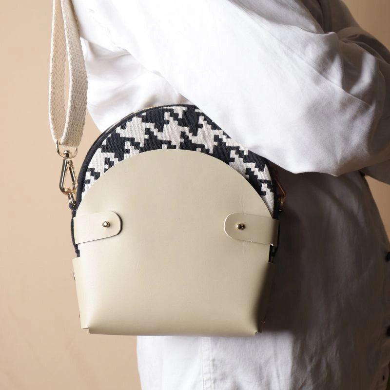 Woman in white shirt carrying around her shoulder a canvas bag with black and white houndstooth weave inside a off-white leather case
