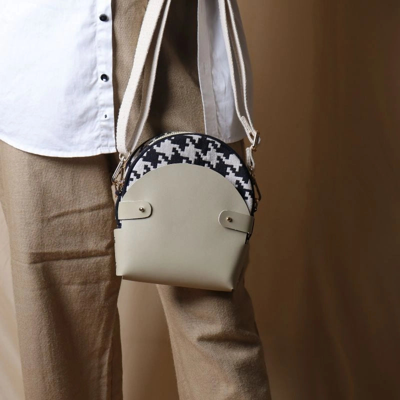 Woman in white shirt and beige pants carrying in her hand a canvas bag with black and white houndstooth weave inside a off-white leather case