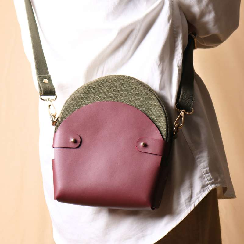 Back View of Woman in a white shirt carrying a dark green canvas crossbody sling in a maroon leather case over her shoulder as a crossbody