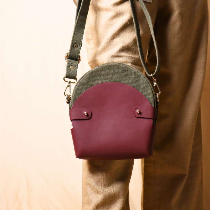 Woman in a white shirt carrying a dark green canvas crossbody sling in a maroon leather case on her hand  as a handbag