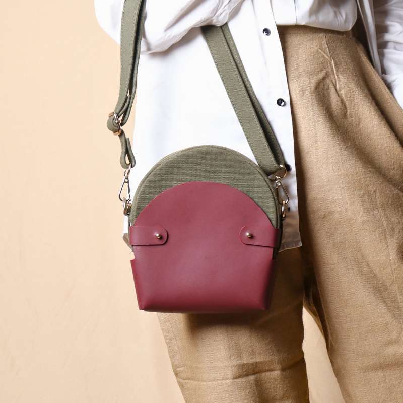 Woman in a white shirt carrying a dark green canvas crossbody sling in a maroon leather case on her hand  as a handbag
