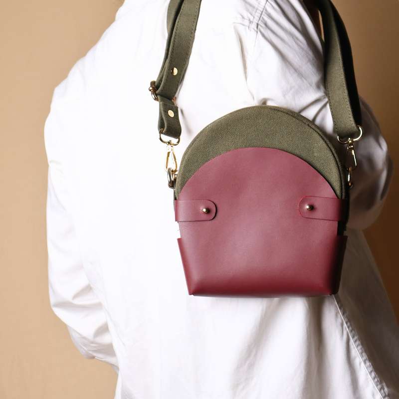 Back View of a Woman in a white shirt carrying a dark green canvas crossbody sling in a maroon leather case over her shoulder