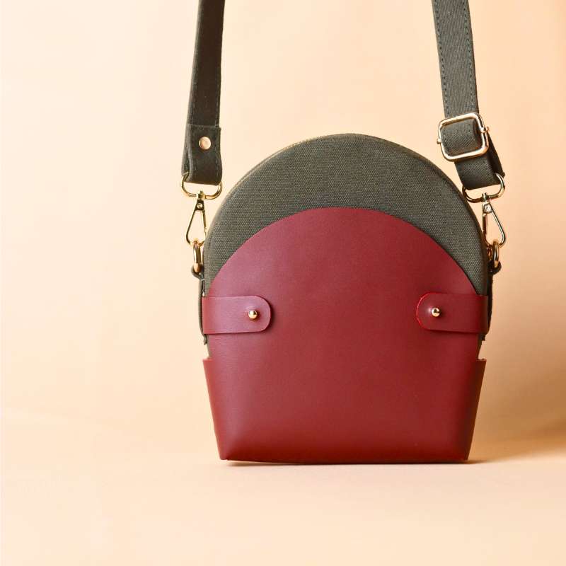 Front view of a Dark Green Canvas Crossbody sling bag in a maroon leather case with its canvas strap extended.