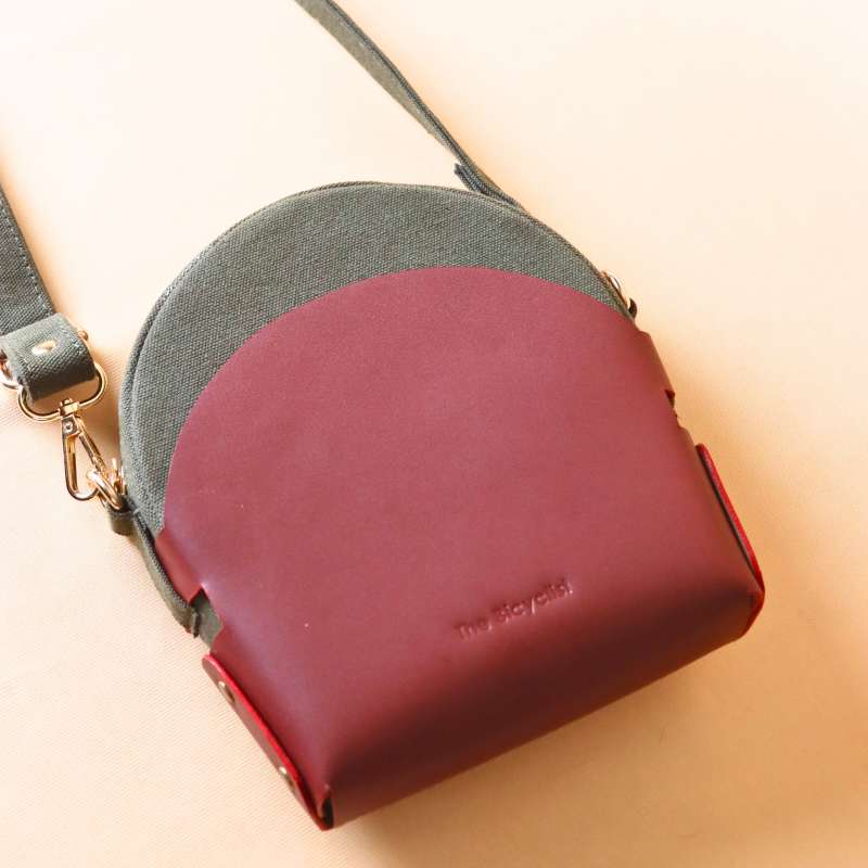 Back view of a Dark Green Canvas Crossbody sling bag in a maroon leather case with its canvas strap extended