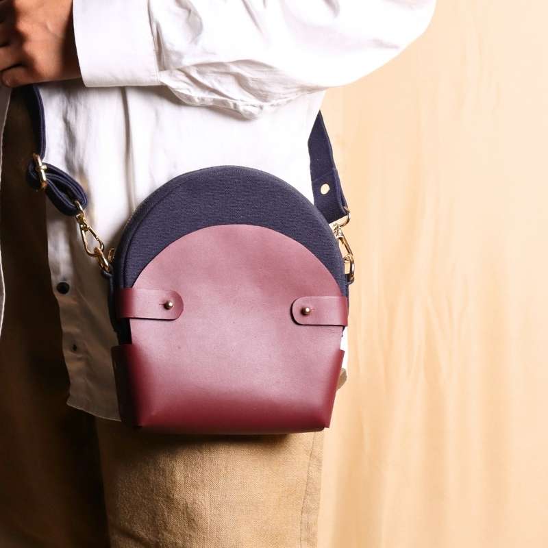 Woman in a white shirt carrying a deep blue canvas crossbody sling in a maroon leather case across her shoulder as a crossbody