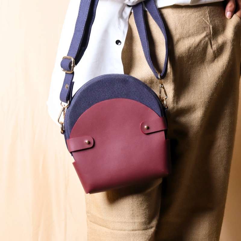 Woman in a white shirt carrying a deep blue canvas crossbody sling in a maroon leather case in her hand a a handbag