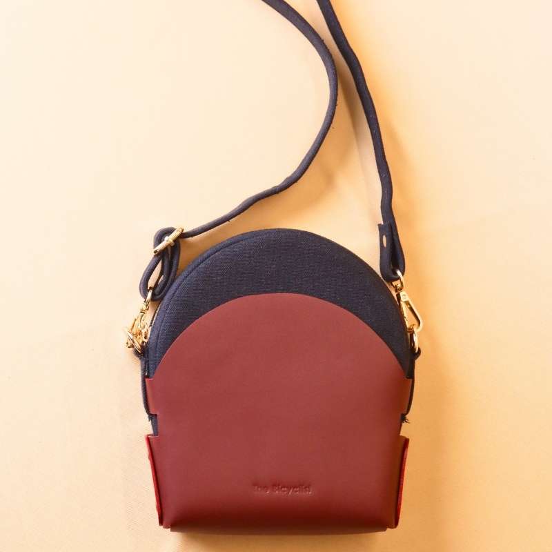 Back view of a Deep Blue Canvas Crossbody sling bag in a maroon leather case with its canvas strap extended