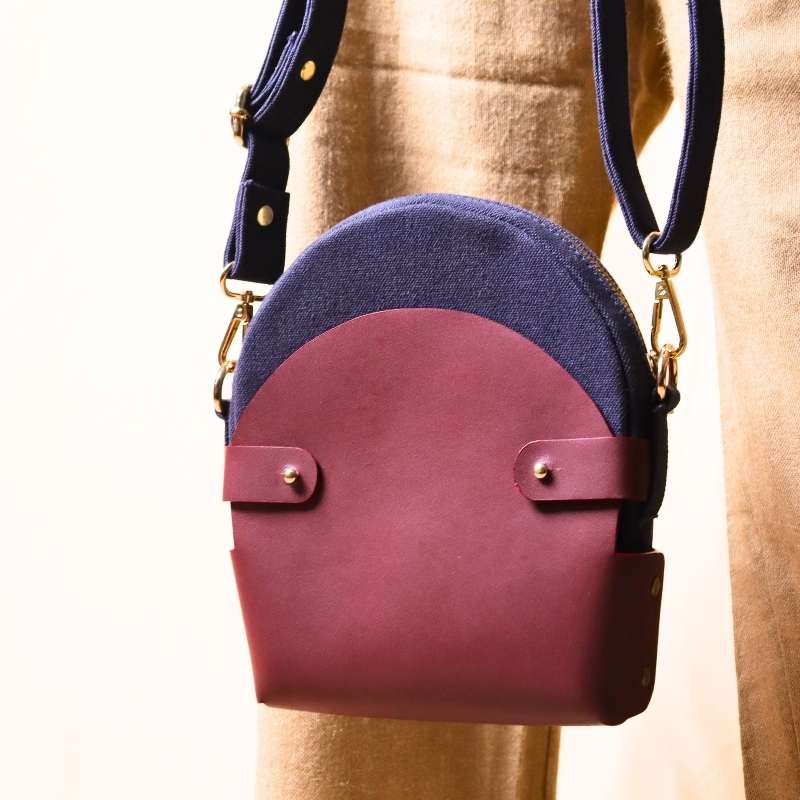 Woman in beige trousers carrying a deep blue canvas crossbody sling in a maroon leather case in her hand