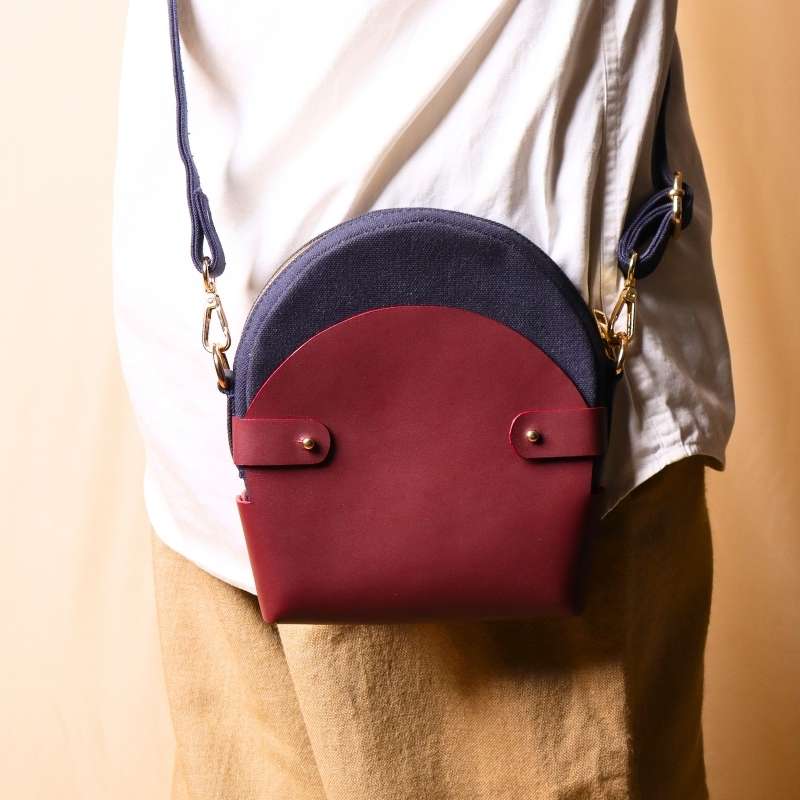 Back View of a Woman in a white shirt carrying a deep blue canvas crossbody sling in a maroon leather case across her shoulder as a crossbody