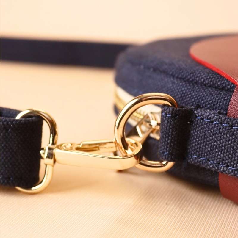 Detailed view of a Gold Metal Fitting on a Deep Blue Canvas Crossbody sling bag in a maroon leather case