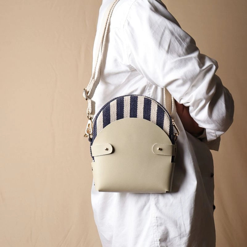 Woman in white shirt carrying around her shoulder a shoulder canvas bag with blue and white stripe weave inside a off-white leather case