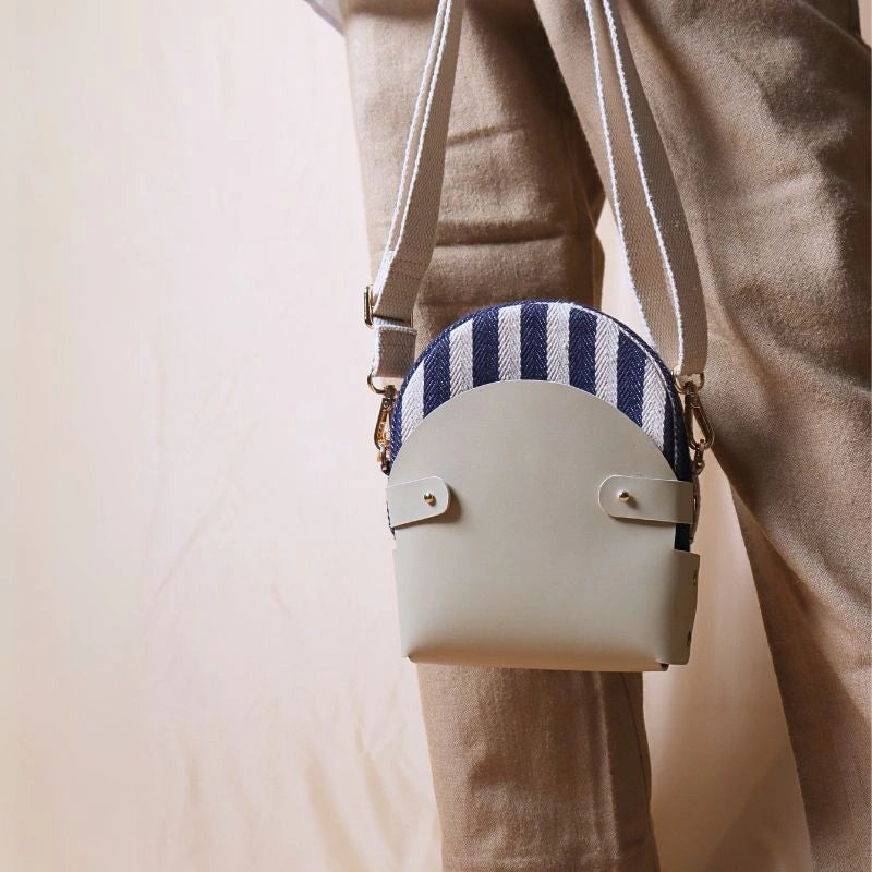 Woman in beige pants carrying a canvas bag with blue and white stripe weave inside a off-white leather case in her hand