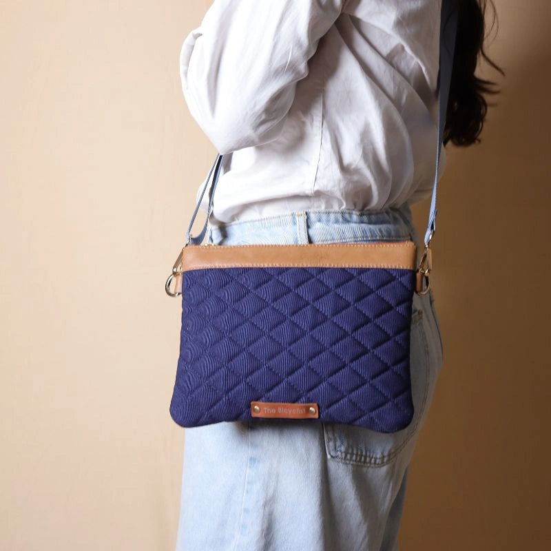 Woman in white shirt carrying a quilted deep blue canvas sling with tan leather trims on her shoulder