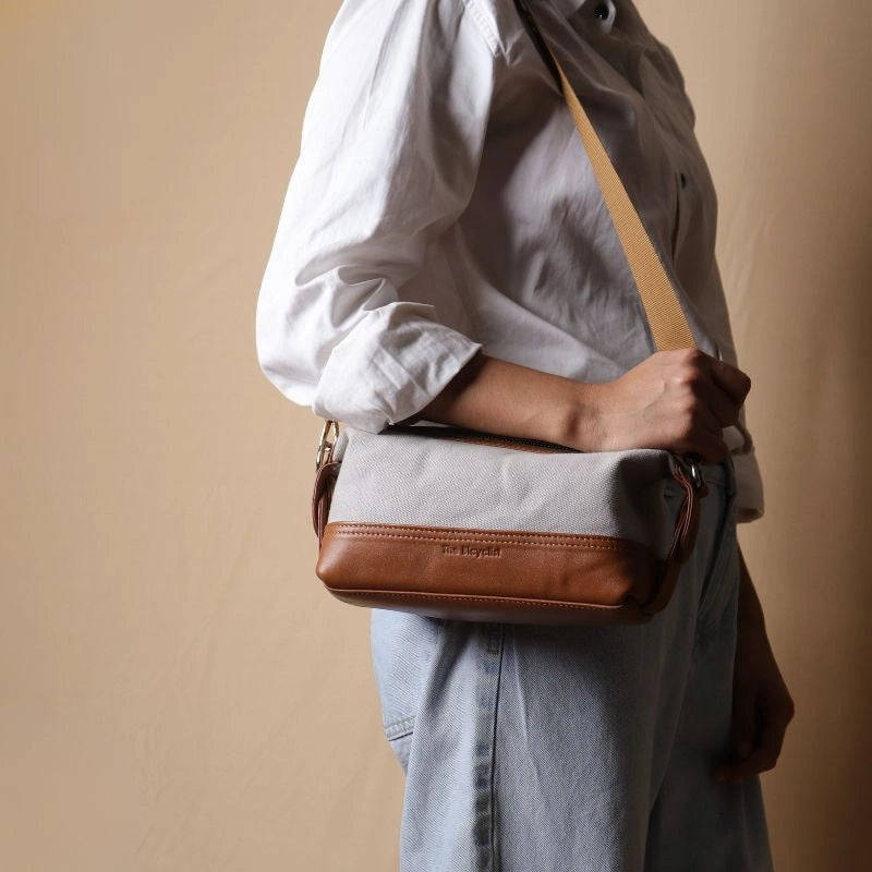 Woman in a white shirt carrying a Grey canvas and tan leather pouch as a side sling on her shoulder