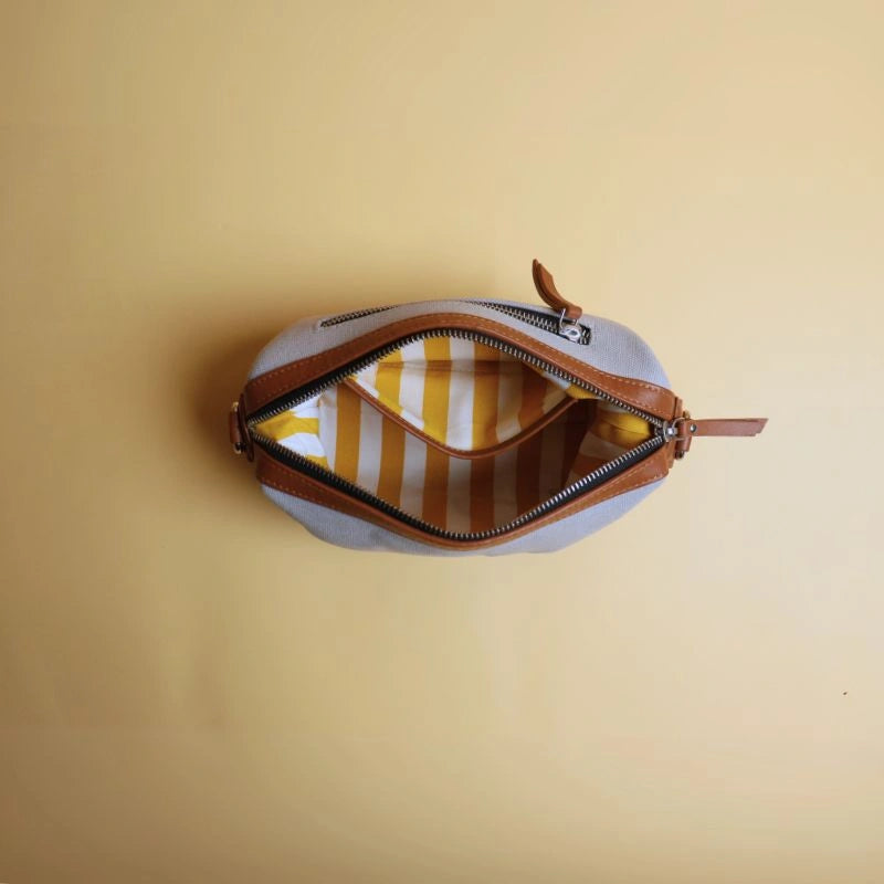 Top Open view of a grey cotton canvas and tan leather dopp kit with metal yellow and white stripe lining and an open pocket