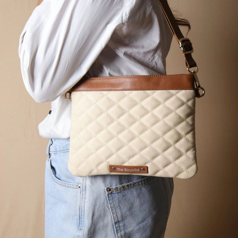 Woman in a white shirt carrying a quilted off-white canvas shoulder bag with tan leather trims and golden hardware