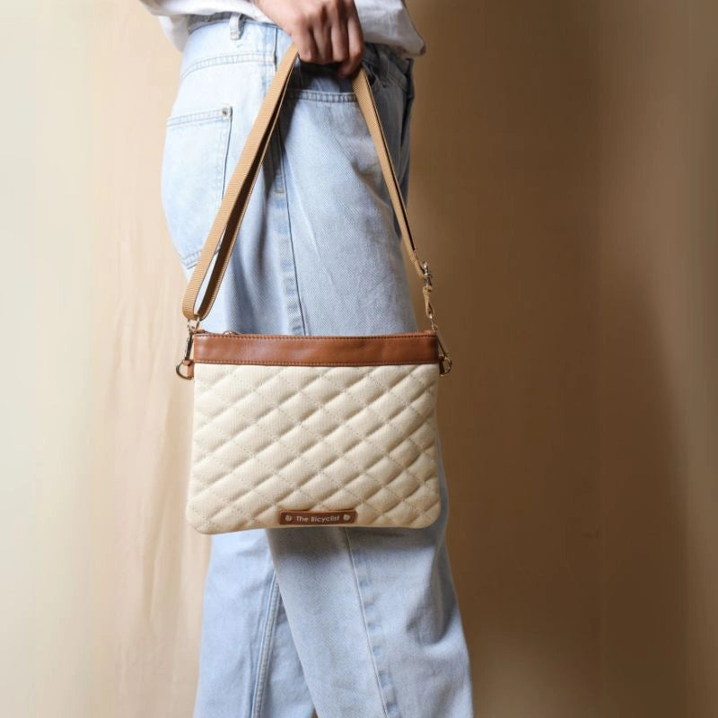 Woman in light blue denims carrying a quilted off-white canvas sling bag with tan leather trims in her had