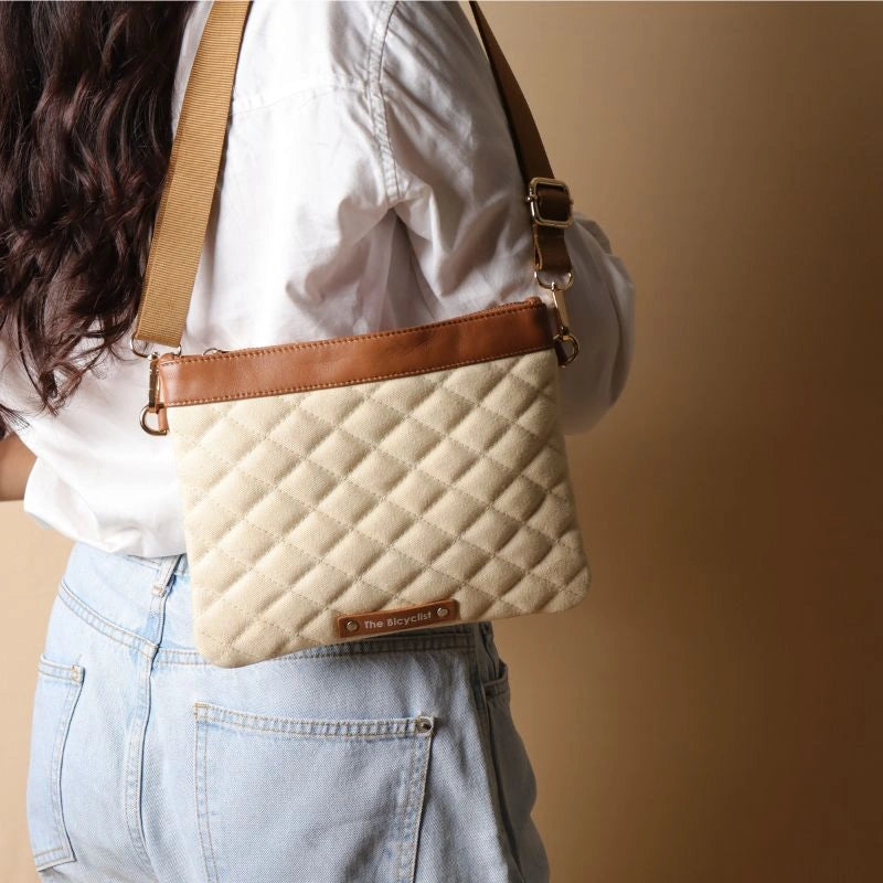 Back view of a woman in a white shirt carrying a quilted_off-white canvas shoulder bag with leather trims over her shoulder.