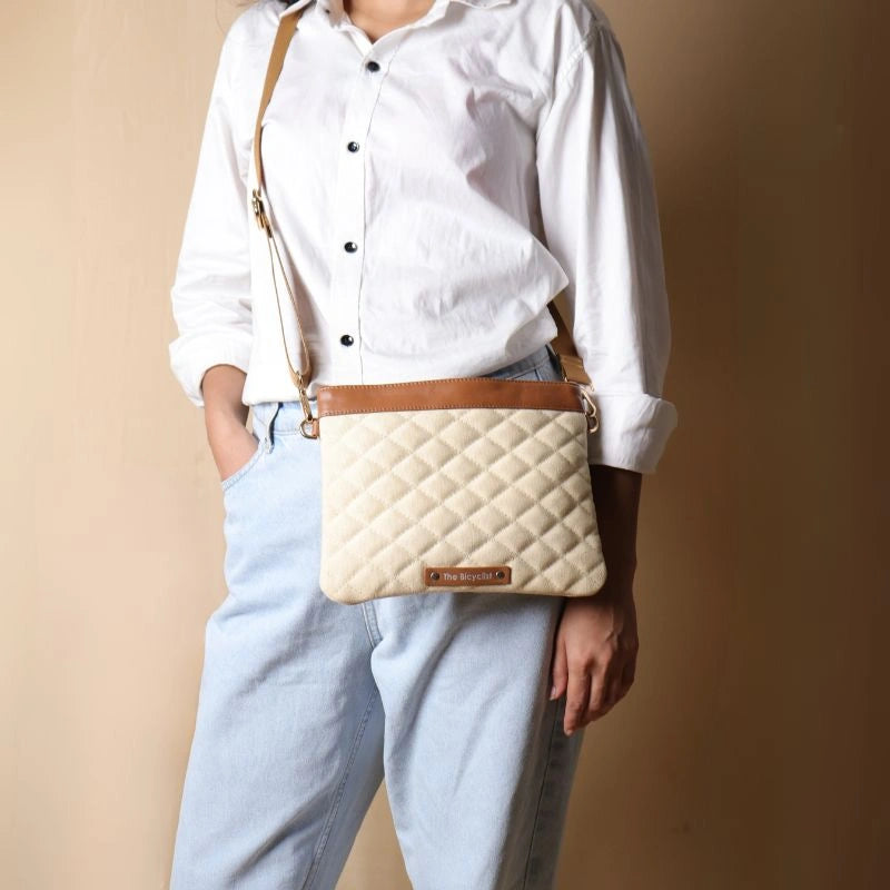 Woman in white shirt carrying a quilted off-white canvas with tan leather trim crossbody pouch bag around her shoulder