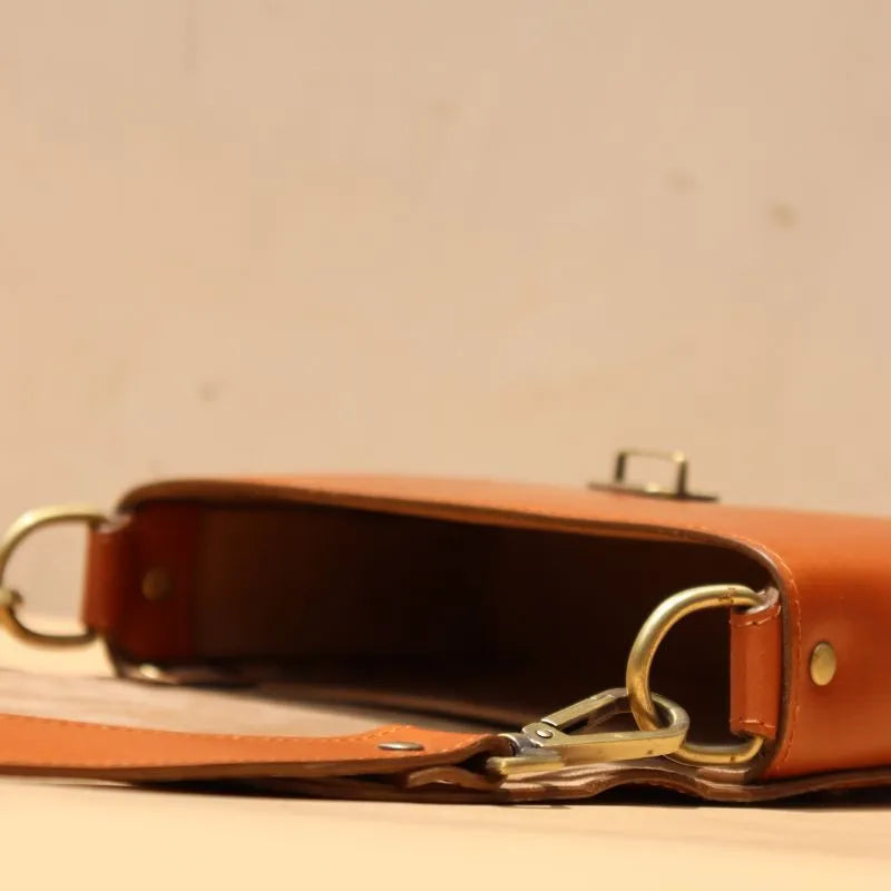 Flat Open image of a Cognac Tan Leather Crossbody sling bag with straps and a flap with a light gold fittings on a peach background