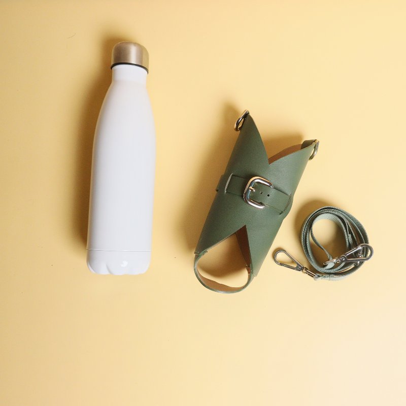 Leather one liter bottle carrier case in Dark Green with chrome plated finish metal fittings and a removable and adjustable nylon strap along with a white bottle front top image with separate bottle and case