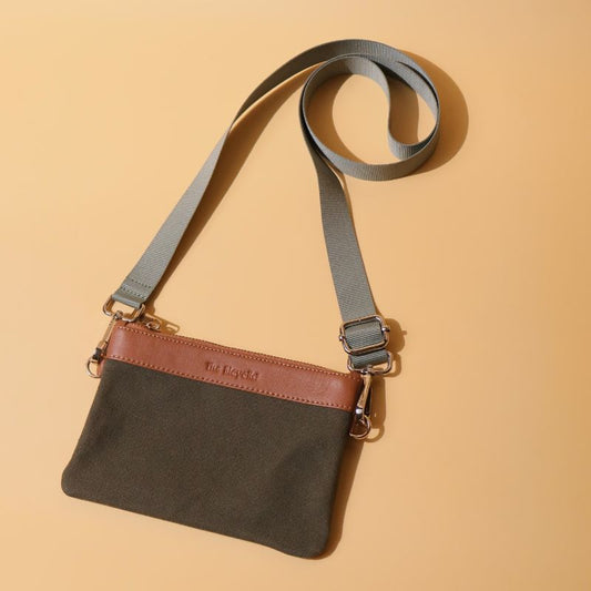 A mini crossbody side sling pouch with removable straps in dark green canvas and tan sheep leather with metal fittings in plated chrome finish