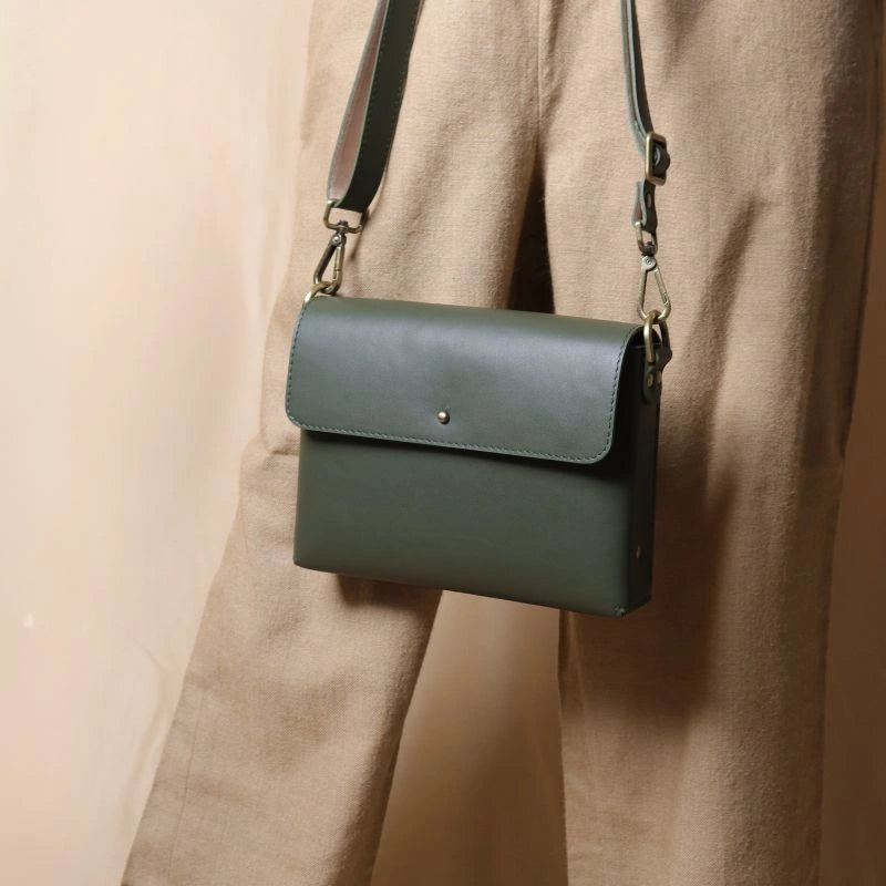 Woman in beige trousers carrying a mint green leather crossbody shoulder side bag with a flap in her hand