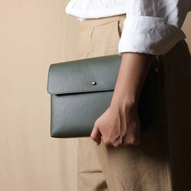 Woman in a white shirt carrying a mint green leather crossbody shoulder side clutch bag with a flap in her hand