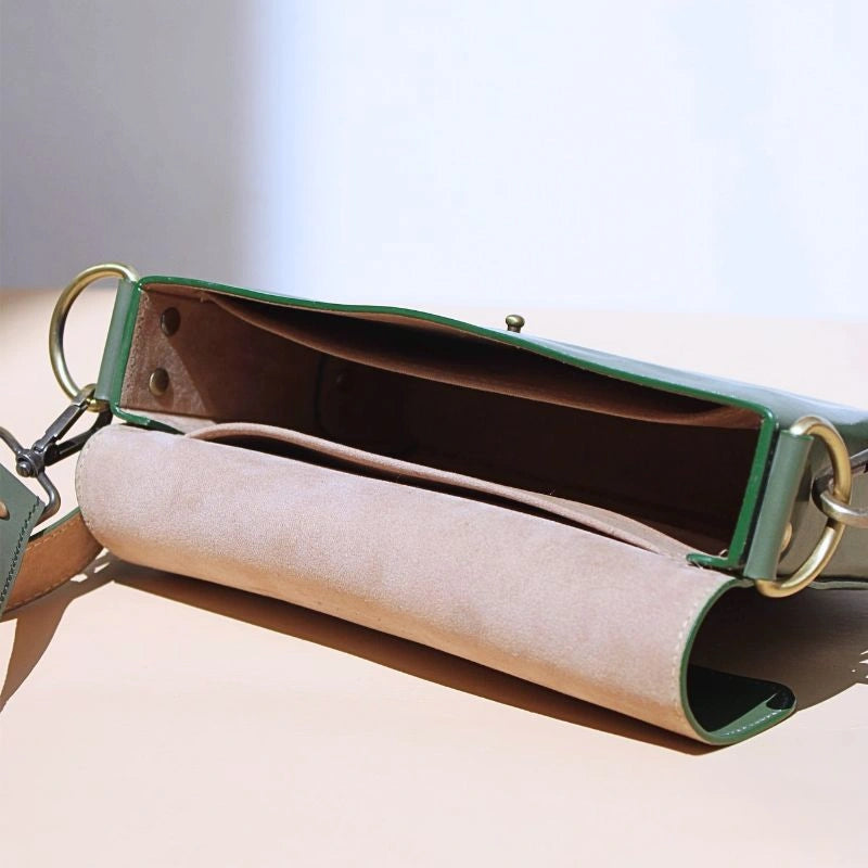 Internal view of a green leather crossbody sling bag with light beige felt lining and two open pockets
