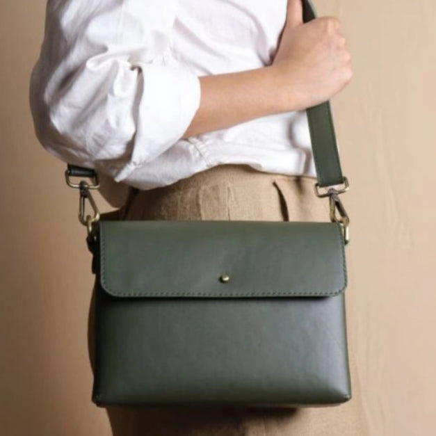Woman in a white shirt carrying a mint green leather crossbody shoulder side bag with a flap around her shoulder